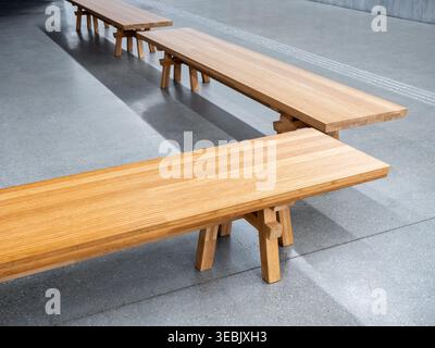 Interni moderni con panche in legno in uno spazio minimalista in cemento, con luce naturale e design pulito, che rappresentano l'architettura, i posti a sedere pubblici, Foto Stock