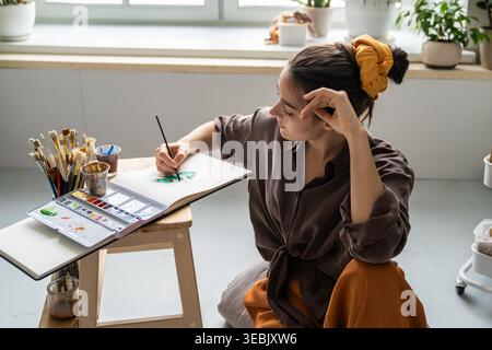 Donna di talento che trascorre del tempo libero con hobby d'arte, dipingendo quadri in un libro di schizzi con aquarelle. Foto Stock
