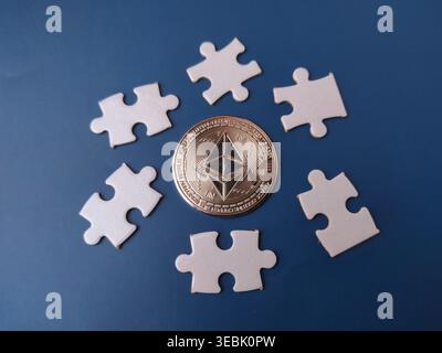 Moneta metallica Ethereum posta al centro di uno sfondo blu. Intorno alla moneta ci sono sei pezzi di puzzle bianchi. Foto Stock