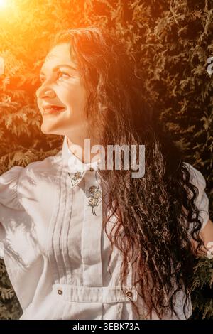 Donna sorridente ritratto di una giovane donna con camicetta ricamata bianca che guarda in giardino Foto Stock