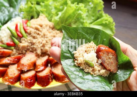 Morso di Sai Krok Planaem, salsicce di maiale alla griglia tailandese con pesce grattugiato e insalata di maiale avvolta in una foglia di Betel selvatico fresca in mano Foto Stock
