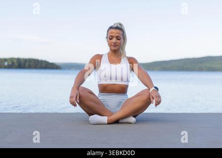 Giovane donna che pratica yoga all'aperto vicino a un lago tranquillo con il tempo caldo Foto Stock