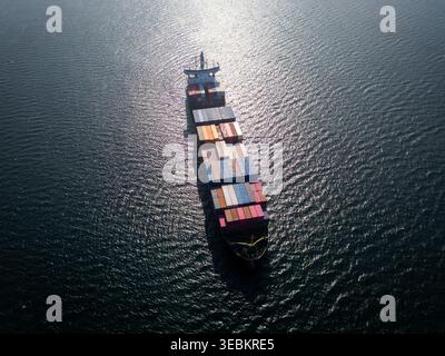 Veduta aerea di una grande nave portacontainer che naviga nell'oceano, forte bagliore del sole Foto Stock