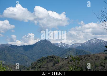 creste verdi e cime innevate sotto un cielo nuvoloso e luminoso Foto Stock