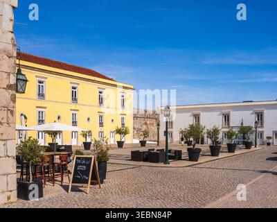 Lisbona, Portogallo - 7 maggio 2022: Vista di una piazza storica soleggiata, con un edificio giallo vibrante e una caffetteria all'aperto sotto un cielo blu brillante. Foto Stock