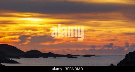Il tramonto dorato risplende sulle linee scure della costa e sulle calme acque dell'oceano Foto Stock