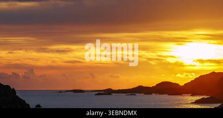 Il tramonto dorato risplende sulle linee scure della costa e sulle calme acque dell'oceano Foto Stock