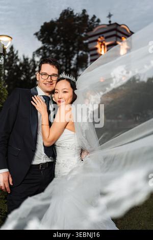 Coppia interrazziale che celebra il giorno del matrimonio con velo scorrevole Foto Stock
