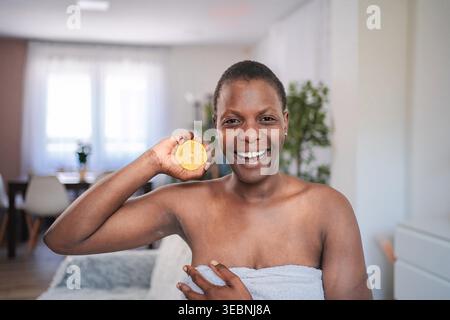 Donna africana felice che tiene una fetta di limone dopo la rasatura per sbiancare la pelle Foto Stock