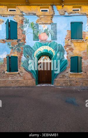 Bologna, Italia - 27 marzo 2022: Veduta di una facciata rustica di un edificio adornata da un vibrante murale di un fiore, con i suoi petali color ottanio che incorniciano una porta di legno sotto Foto Stock