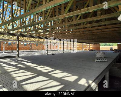 Ampia visuale del sistema di travi a capriate in legno installato sul grande pavimento dell'edificio con ombre e supporti strutturali. Edilizia, carpenteria, architettura, Foto Stock