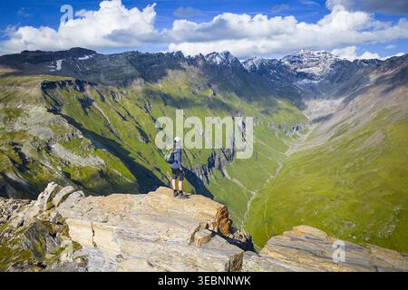 Vista aerea di un escursionista solitario che si staglia contro la vallata verde e le cime innevate di Schareck, Nationalpark alti Tauri, Carinzia, Aus Foto Stock