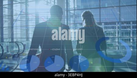 Portare due professionisti in tute che si spostano attraverso l'atrio di vetro con grafici dati sovrapposti Foto Stock