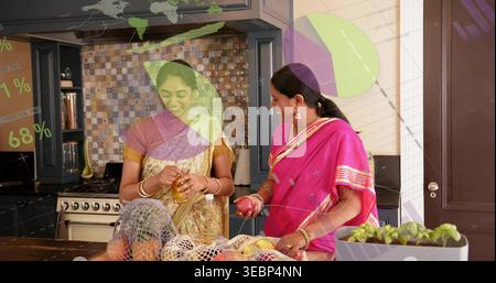 Preparare due donne indiane in sari dorati e rosa maneggiando melograno a Kitchen Island, con barattolo Foto Stock