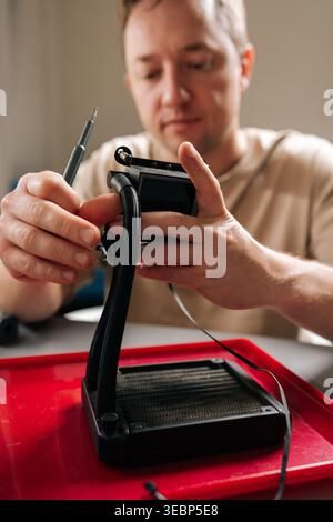 Man si è concentrato sulla riparazione del sistema di raffreddamento a liquido smontato per computer, tenendo le parti della pompa e del radiatore mentre si lavora su cavi e collegamenti Foto Stock