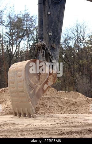Primo piano di una benna dell'escavatore con denti su terreno sabbioso. Attrezzature da costruzione professionali per movimento terra. Vista dettagliata della parte di lavoro Foto Stock