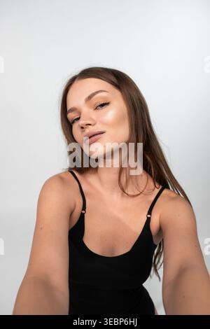 Giovane donna che scatta un selfie, cattura la sua bellezza naturale e la sua pelle fresca, posa casualmente in uno studio Foto Stock