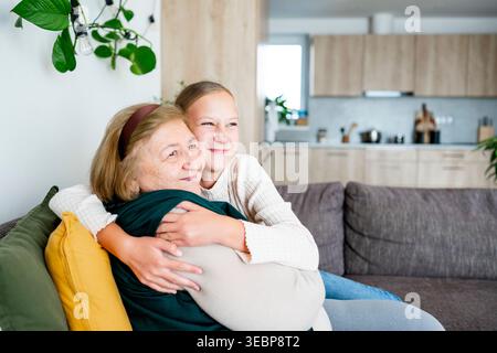 Nipote che abbraccia la nonna in un caldo ritratto di famiglia a casa. Foto Stock