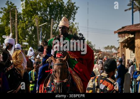 Città di Zaria, Nigeria - 22 marzo 2026: Vista di una figura regale in verde vivace e cremisi, in cima a un cavallo riccamente ornato, in mezzo a un processio soleggiato Foto Stock