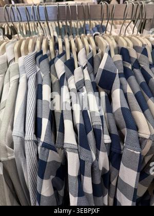 Camicie a scacchi piegate nelle tonalità blu, grigio e bianco esposte su grucce in un negozio. Foto mobile Foto Stock