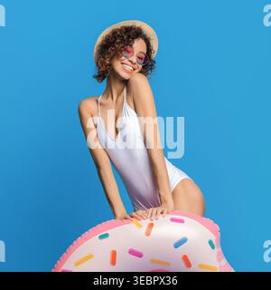 Giorno estivo luminoso con una giovane donna che posa su un galleggiante colorato vicino a uno sfondo blu Foto Stock