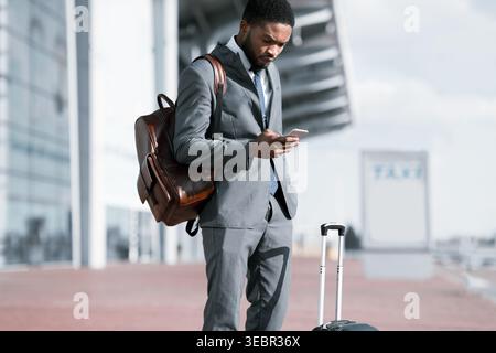 Il viaggiatore d'affari controlla il telefono mentre aspetta all'aeroporto per il prelievo in taxi Foto Stock