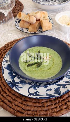 Zuppa cremosa di asparagi verdi servita in porcellana blu. L'elegante tendenza culinaria mediterranea combina texture organiche con tradizionali motivi floreali Foto Stock