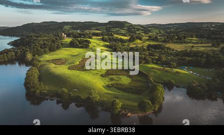 Questa splendida foto aerea cattura un tranquillo paesaggio con un lago, colline ondulate e un castello storico in lontananza Foto Stock