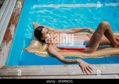 Vista dall'alto della giovane donna in piscina all'aperto sul letto galleggiante, rilassante. Foto Stock