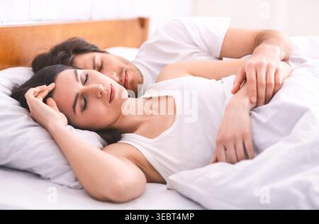Coppia che riposa tranquillamente nel letto con morbide lenzuola bianche durante una mattinata tranquilla Foto Stock