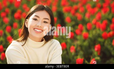 Una donna sorridente posa tra i vivaci fiori rossi in un giorno di sole in un giardino Foto Stock