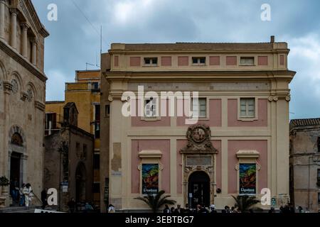 Il Palazzo di Città a Cagliari presenta una facciata rosa e crema con uno stemma. Sorge su Piazza Palazzo sotto un cielo nuvoloso con gente nelle vicinanze. Foto Stock