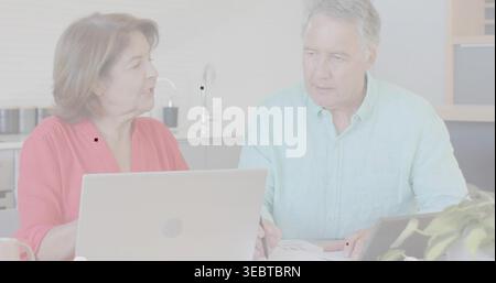 Revisione di documenti uomo in camicia verde e donna in camicia corallina in cucina con computer portatili Foto Stock