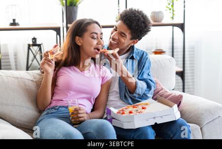 La coppia ama la pizza insieme su un accogliente divano in un moderno soggiorno durante una serata informale Foto Stock