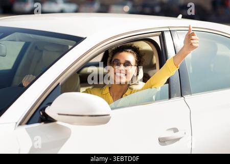 Donna sorridente e che regala pollice mentre è seduta in macchina durante il giorno di sole Foto Stock