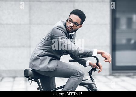 Uomo elegante in tuta in bicicletta su Urban Street durante il giorno Foto Stock