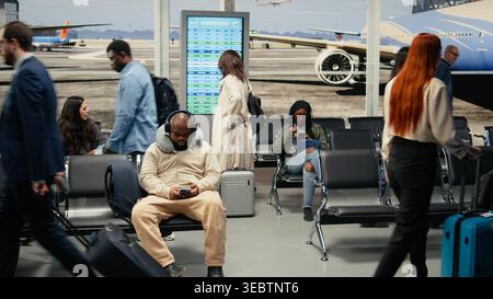 Una folla diversificata di turisti in aeroporto che trasportano carrelli, tornano a casa per le vacanze. Persone che trasportano bagagli nel terminal delle partenze affollato durante il viaggio internazionale, in attesa dell'arrivo dell'aereo, fotocamera A. Foto Stock
