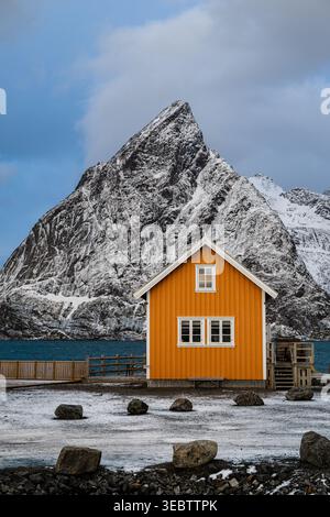 Piccola casa gialla di fronte a una montagna nel villaggio di Hamnoy nelle isole Lofoten Foto Stock