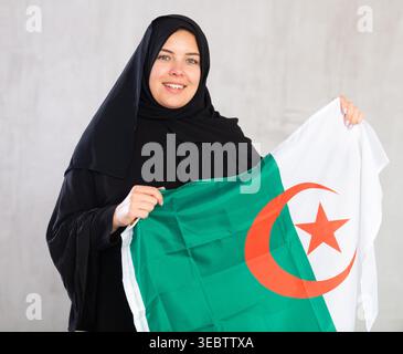 Felice giovane donna vestita con abiti tradizionali islamici con bandiera algerina Foto Stock