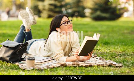 Giovane donna che si gode un libro mentre si rilassa sull'erba in un parco in una giornata di sole Foto Stock