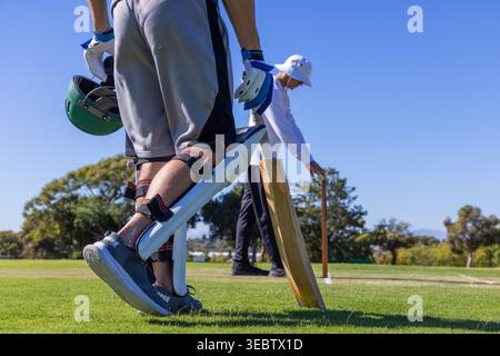 Due giocatori di cricket maschi in piedi sul campo di erba, batter in palle che tengono il casco e pipistrello vicino a ceppi Foto Stock