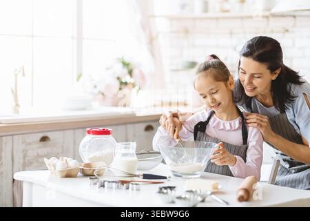 Mamma e figlia si divertono a cucinare insieme in una cucina luminosa mentre preparano una ricetta Foto Stock