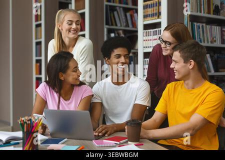 Gruppo di studenti che collaborano intorno a un notebook in un ambiente di libreria Foto Stock
