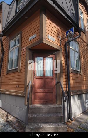 HELSINKI, FINLANDIA - 11 AGOSTO 2025: Vista ravvicinata dell'ingresso di un edificio in legno con una porta rossa scuro e gradini in pietra in estate. Foto Stock