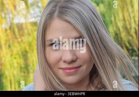 Colpo alla testa di una giovane donna con capelli biondi chiari e occhi blu all'aperto con luce naturale Foto Stock