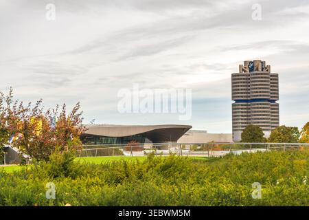 L'edificio dello showroom BMW Welt e l'iconica torre della sede centrale BMW a quattro cilindri vista dall'Olympiapark con il fogliame autunnale in primo piano, Monaco di Baviera Foto Stock
