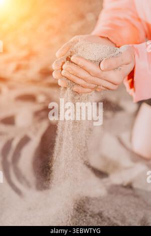 Mani di sabbia che versano. Una donna versa una manciata di sabbia asciutta da palmi ricoperti sotto la calda luce del sole che rappresenta il tempo o la perdita. Foto Stock