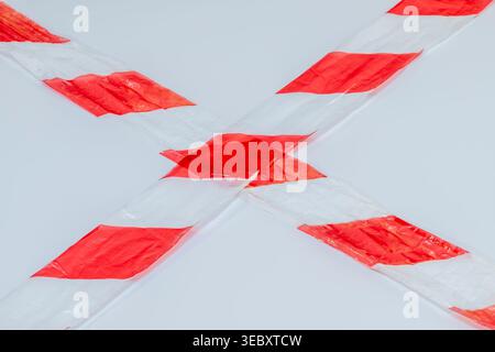 Due pezzi di nastro a strisce rosse e bianche, utilizzati per lavori stradali, chiamati nastro segnaletico o nastro barriera, sono posizionati in una croce X su uno sfondo bianco Foto Stock