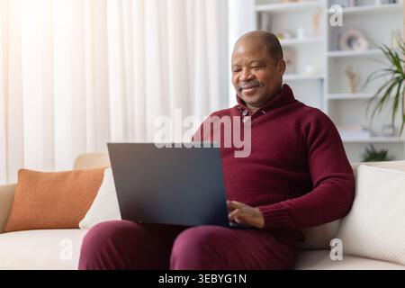 Uomo afroamericano maturo seduto sul divano usando un computer portatile a casa Foto Stock