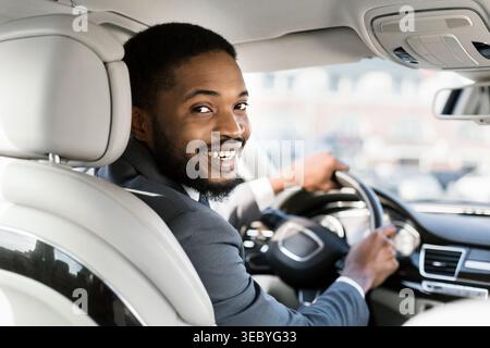 Autista sorridente in tuta alla guida di un veicolo di lusso in un ambiente urbano Foto Stock